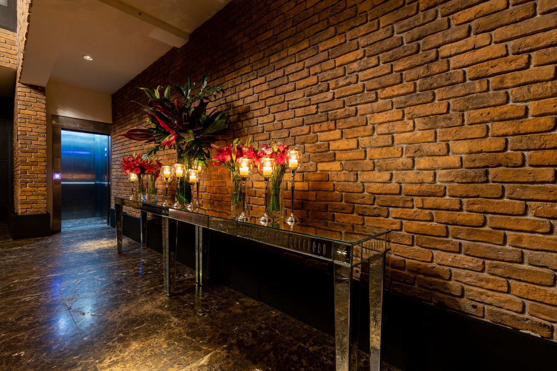 Sophisticated interior featuring a red brick wall, elegant candles, and floral arrangements.
