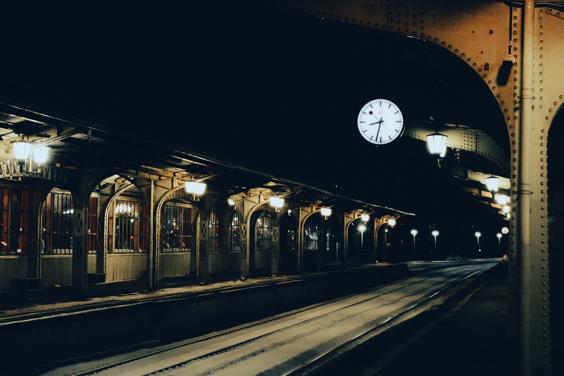 A dimly lit train station platform during nighttime with an illuminated clock.