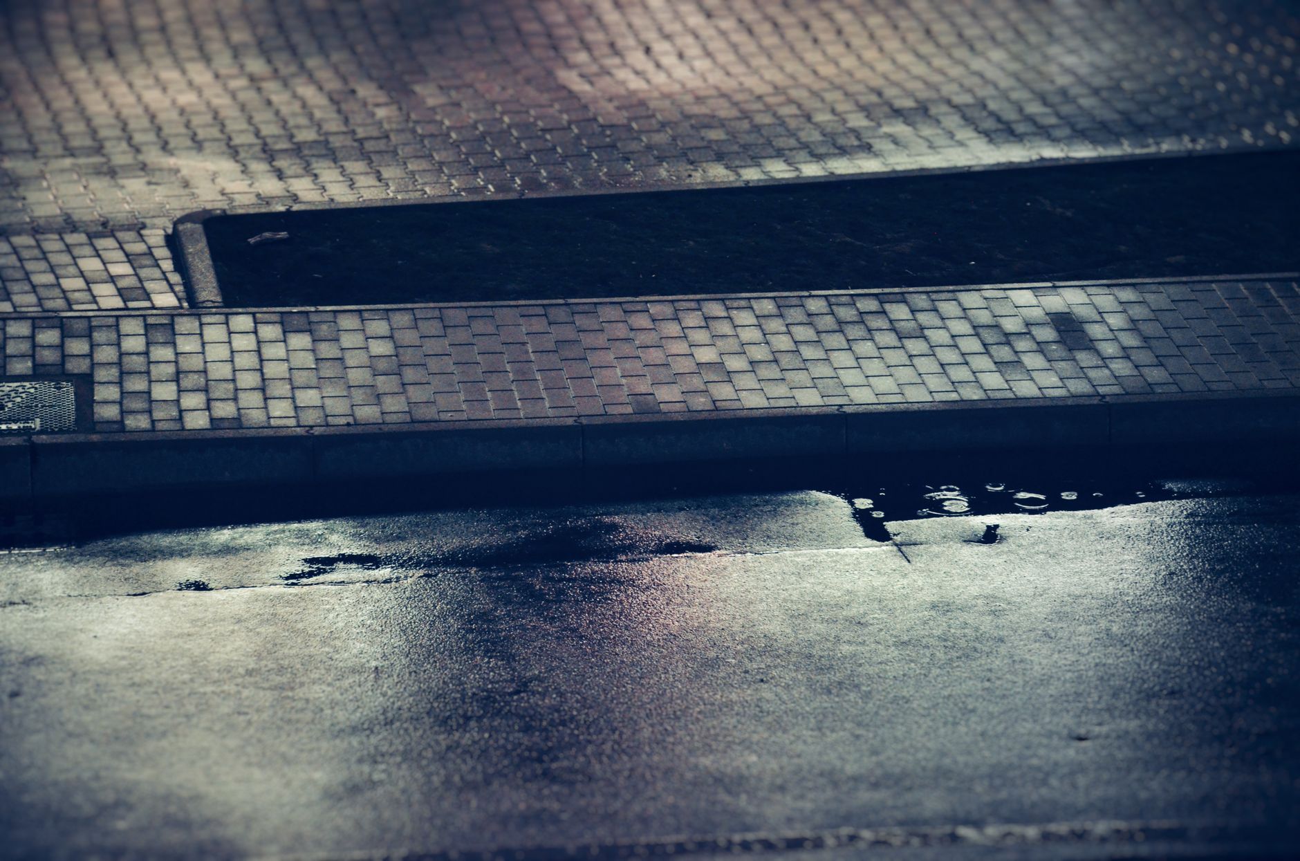 Moody evening scene of a wet city sidewalk reflecting soft light, captured at twilight.